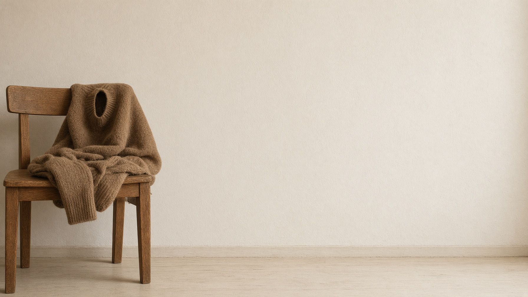 A cream plaster wall. A brown wool sweater sits on a wooden chair. A quiet balloon waits.