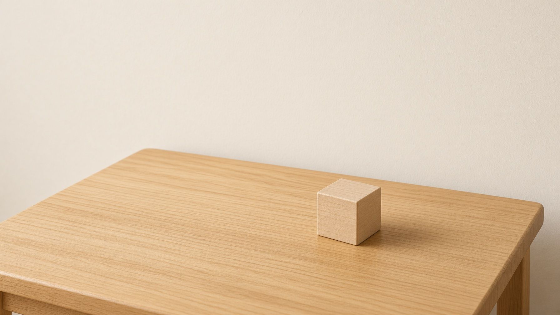 A maple table under a quiet cream wall. A rubber ball waits in the air. A wooden cube sits still.